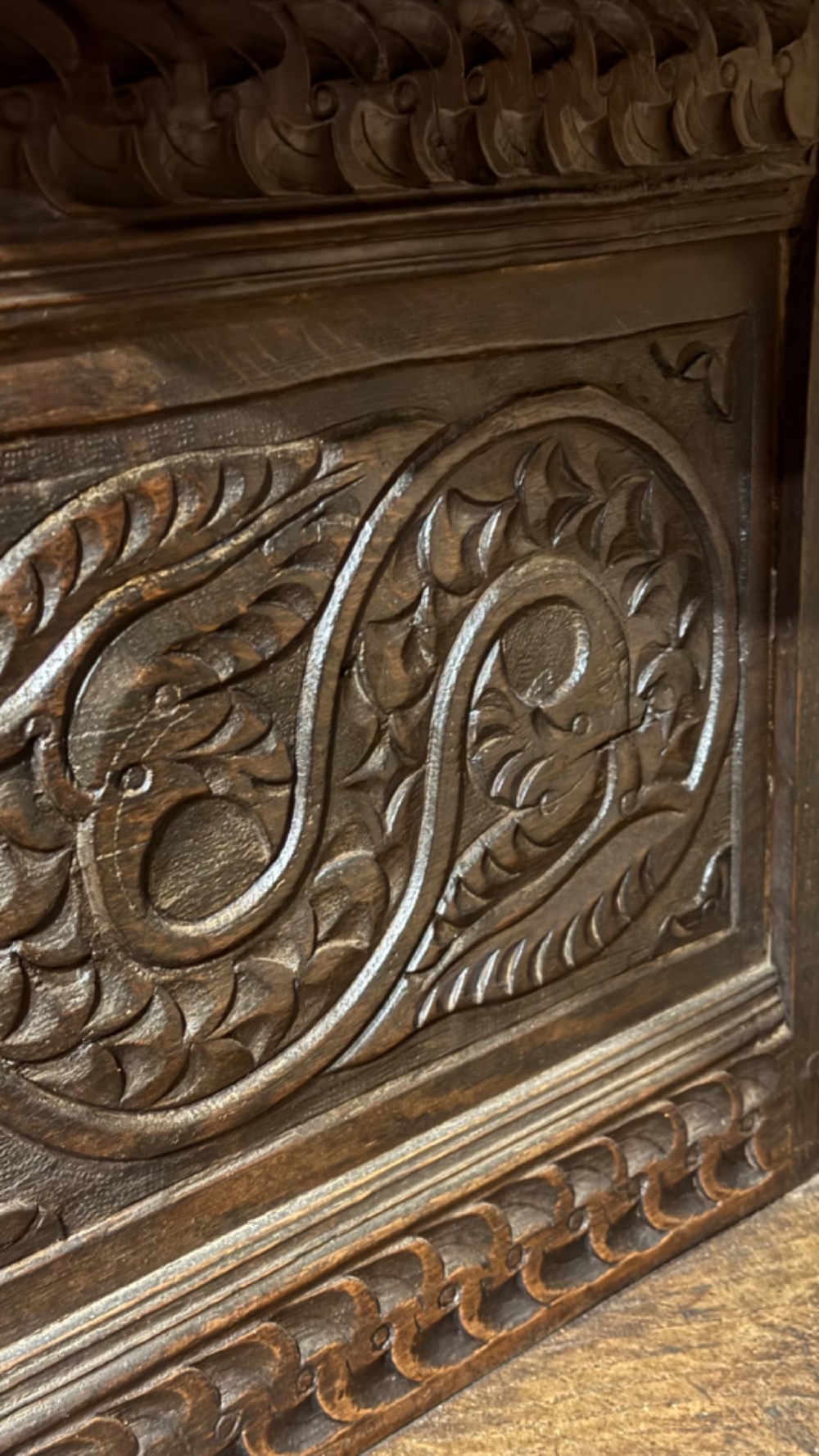 A 17th-century style dark carved oak livery cupboard featuring ornate relief carving, a central face motif panel, turned supports, and an open lower shelf. View X