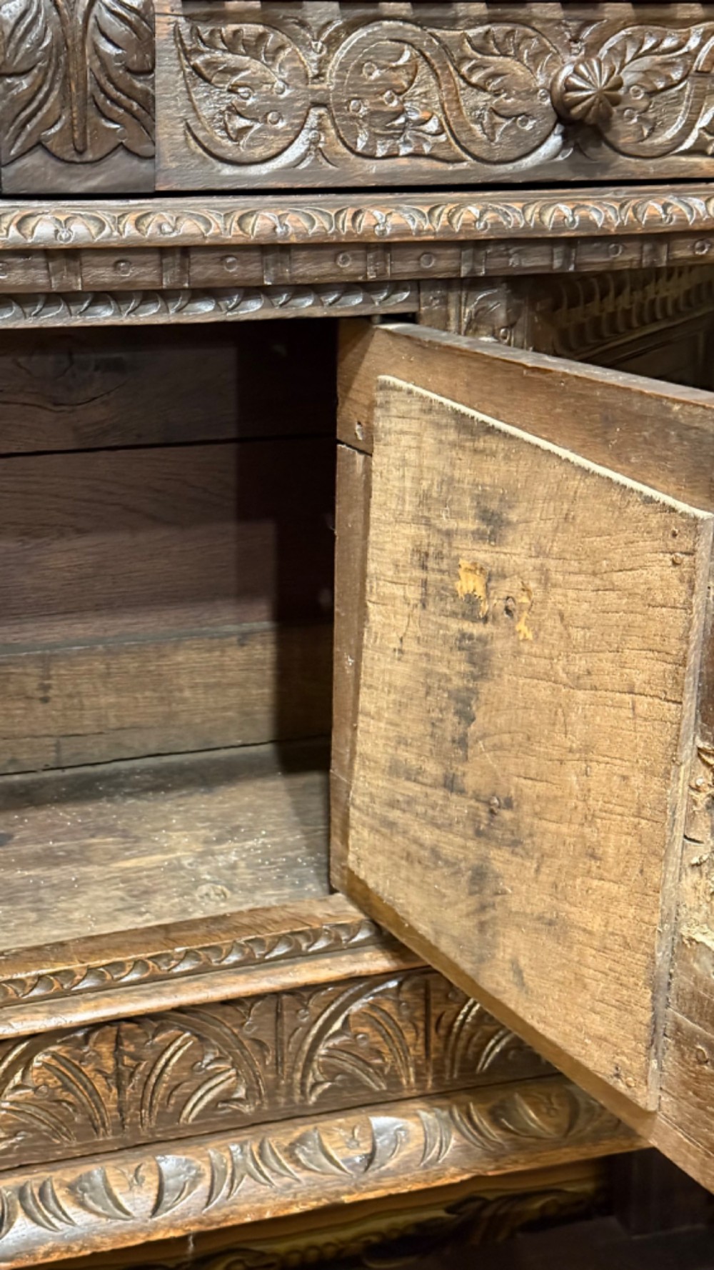 A 17th-century style dark carved oak livery cupboard featuring ornate relief carving, a central face motif panel, turned supports, and an open lower shelf. View XIII