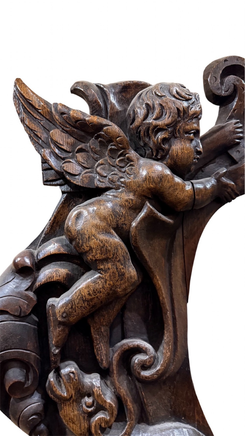 An 18th century dark carved oak wall mirror featuring carved cherubs and scrolling motifs framing an oval mirror plate. View III