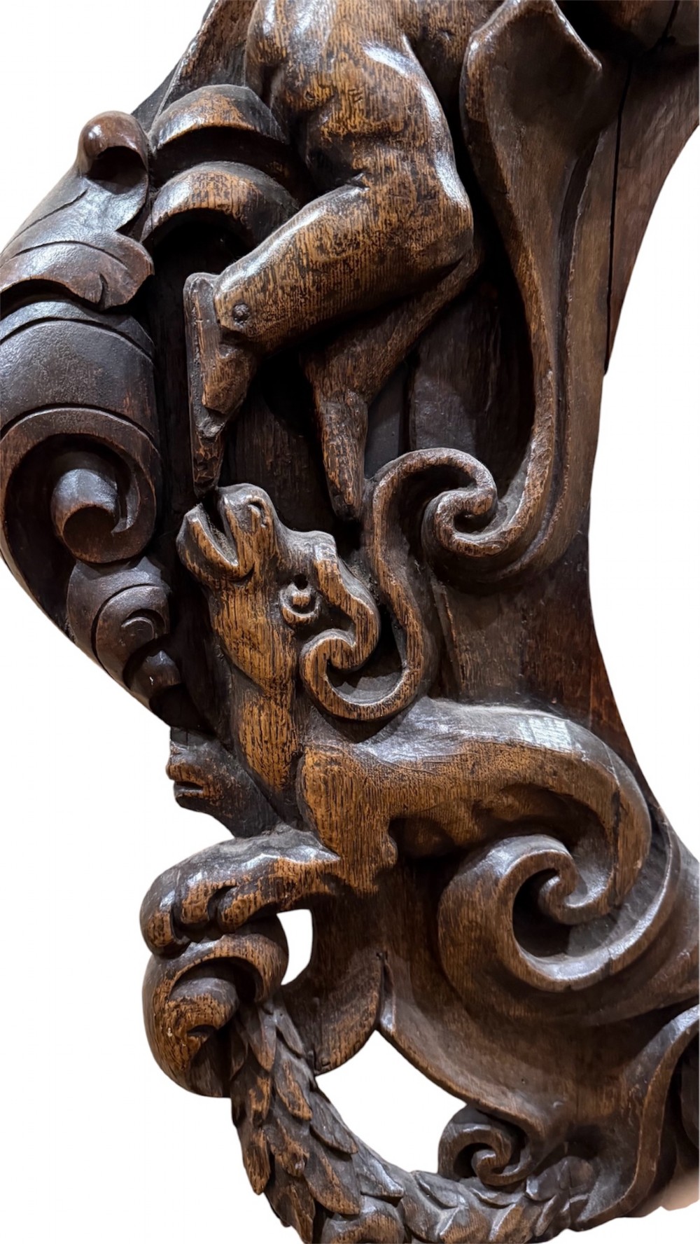 An 18th century dark carved oak wall mirror featuring carved cherubs and scrolling motifs framing an oval mirror plate. View V
