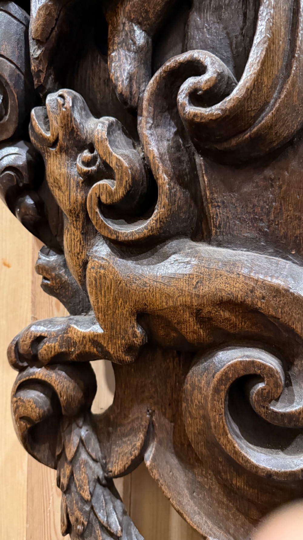 An 18th century dark carved oak wall mirror featuring carved cherubs and scrolling motifs framing an oval mirror plate. View VII