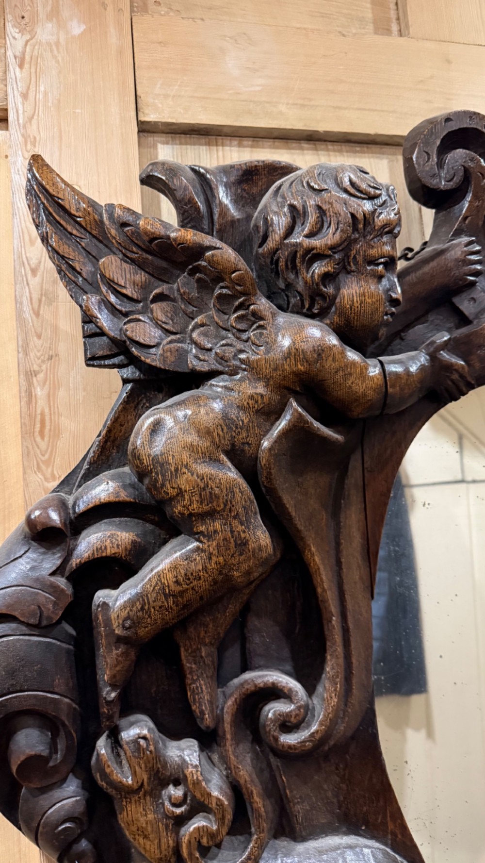 An 18th century dark carved oak wall mirror featuring carved cherubs and scrolling motifs framing an oval mirror plate. View IX