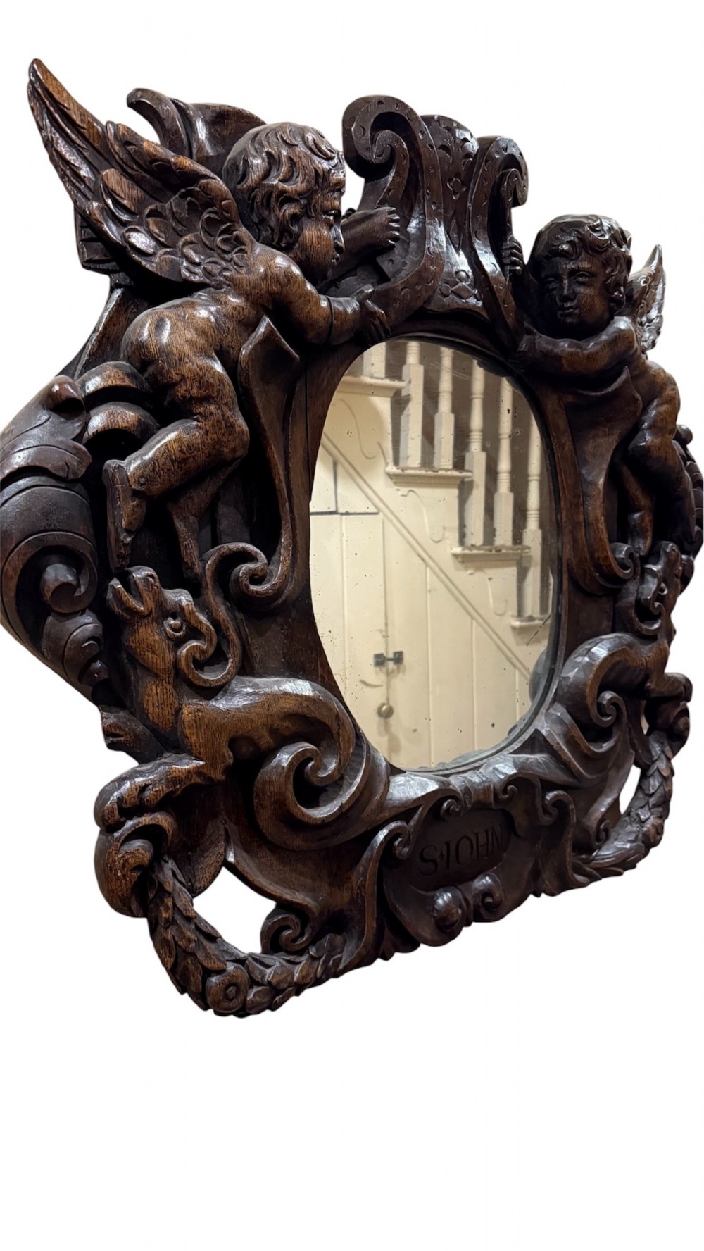 An 18th century dark carved oak wall mirror featuring carved cherubs and scrolling motifs framing an oval mirror plate. View XI