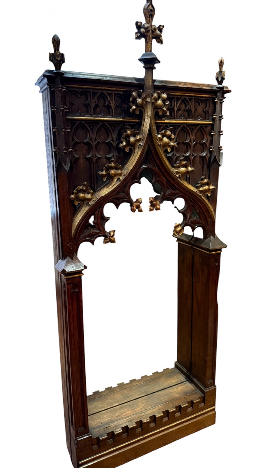 A dark carved oak Gothic Revival mirror frame featuring a pointed arch, intricate tracery, gilded crockets, and decorative finials.