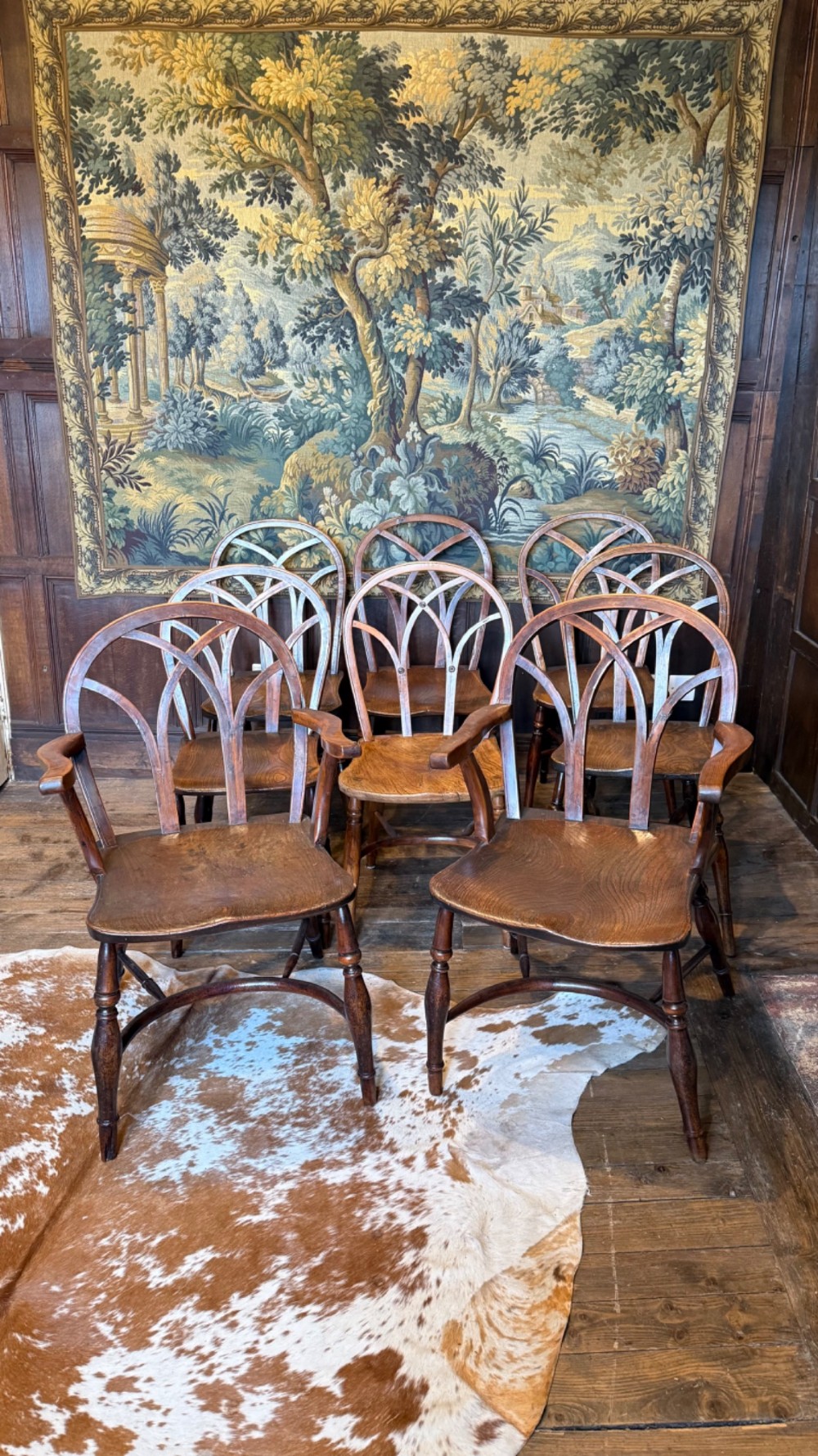 A set of 19th-century Gothic Windsor wooden dining chairs featuring pointed arch back splats, saddle seats, and turned legs.
