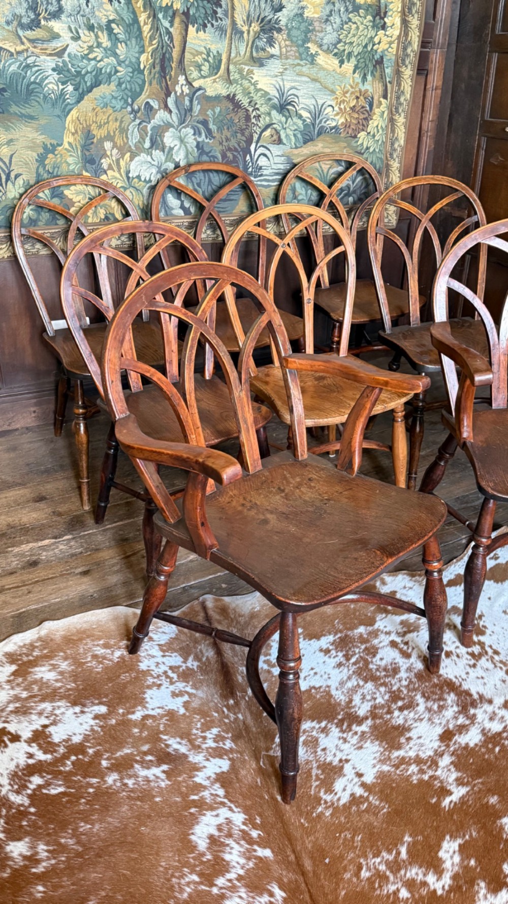 A set of 19th-century Gothic Windsor wooden dining chairs featuring pointed arch back splats, saddle seats, and turned legs. View IV