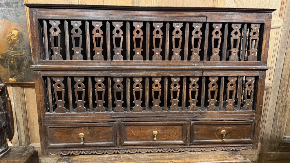 A dark oak seventeenth-century hanging cupboard featuring two upper tiers with carved pierced balusters and three small drawers with teardrop handles along the base.
