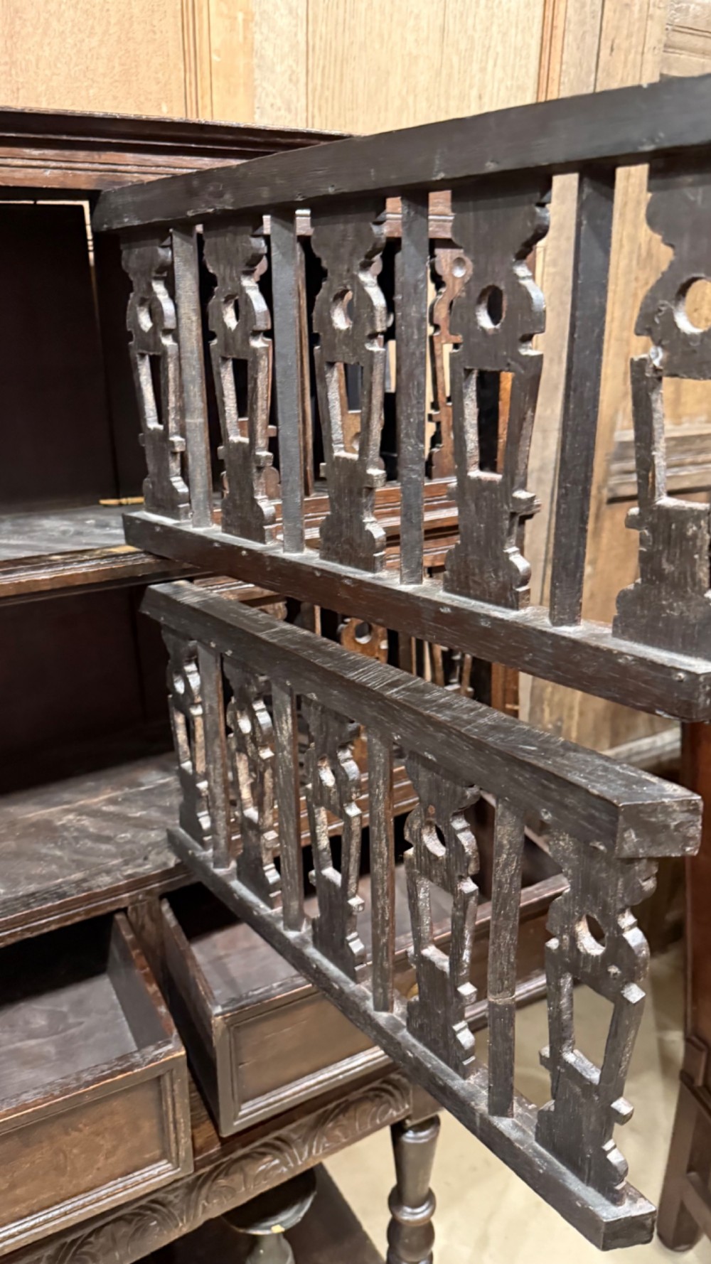 A dark oak seventeenth-century hanging cupboard featuring two upper tiers with carved pierced balusters and three small drawers with teardrop handles along the base. View VII