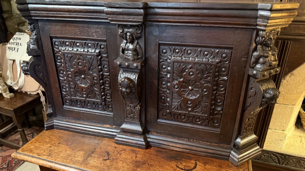 An 18th-century dark oak hanging cupboard featuring carved figural columns, relief door panels with floral motifs, and carved masks.