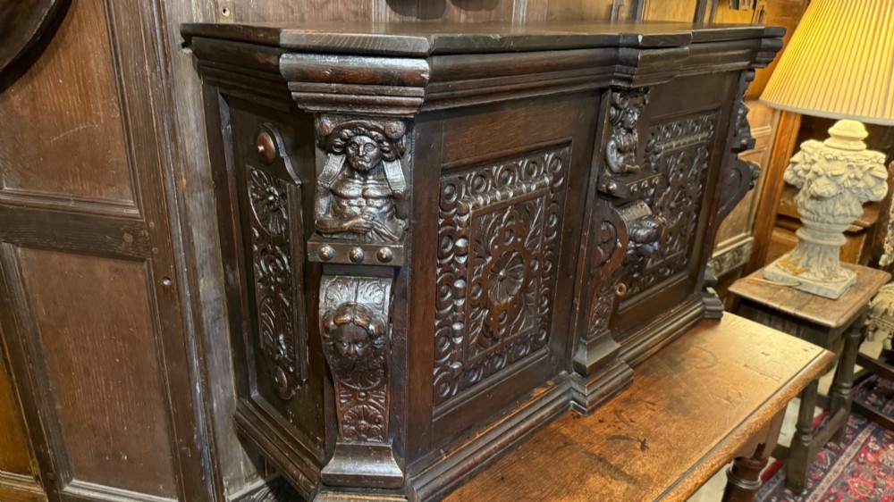 An 18th-century dark oak hanging cupboard featuring carved figural columns, relief door panels with floral motifs, and carved masks. View II