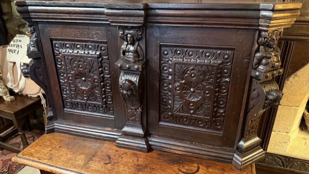 An 18th-century dark oak hanging cupboard featuring carved figural columns, relief door panels with floral motifs, and carved masks. View III