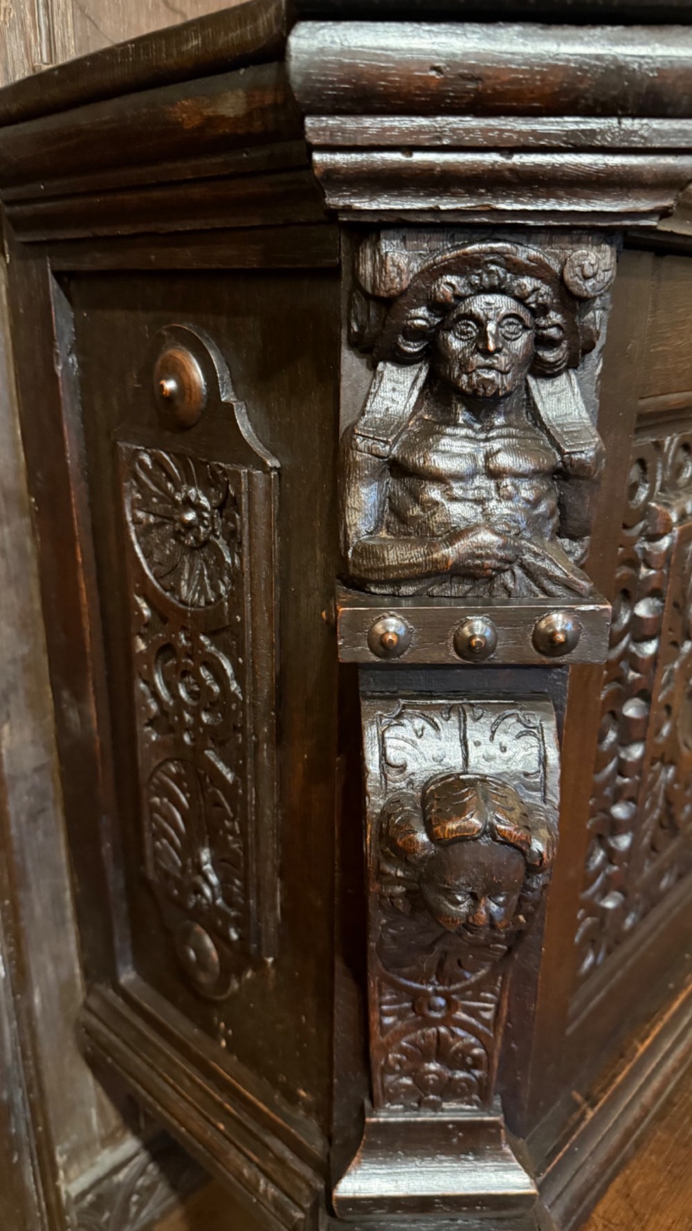 An 18th-century dark oak hanging cupboard featuring carved figural columns, relief door panels with floral motifs, and carved masks. View V