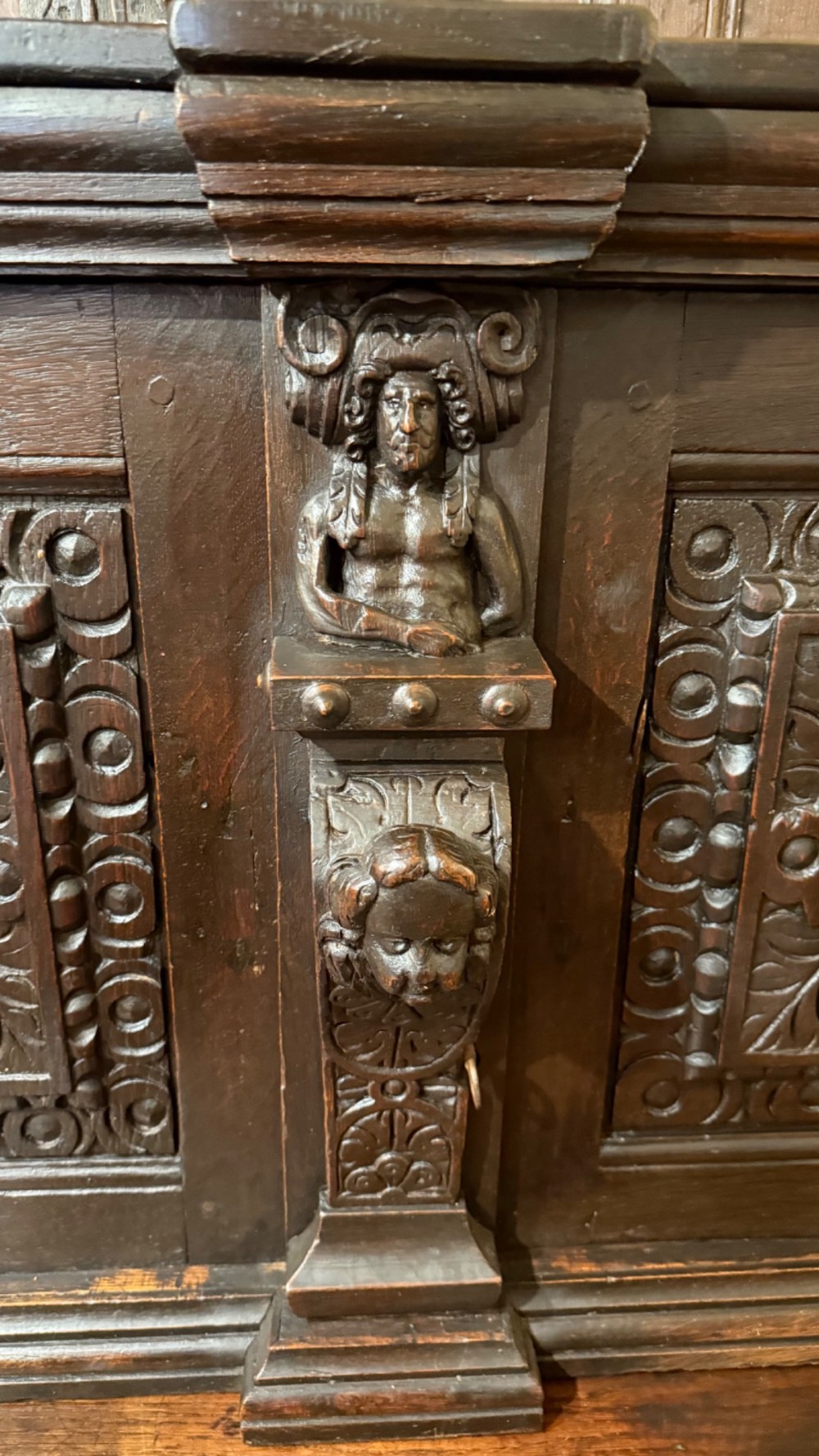 An 18th-century dark oak hanging cupboard featuring carved figural columns, relief door panels with floral motifs, and carved masks. View VI