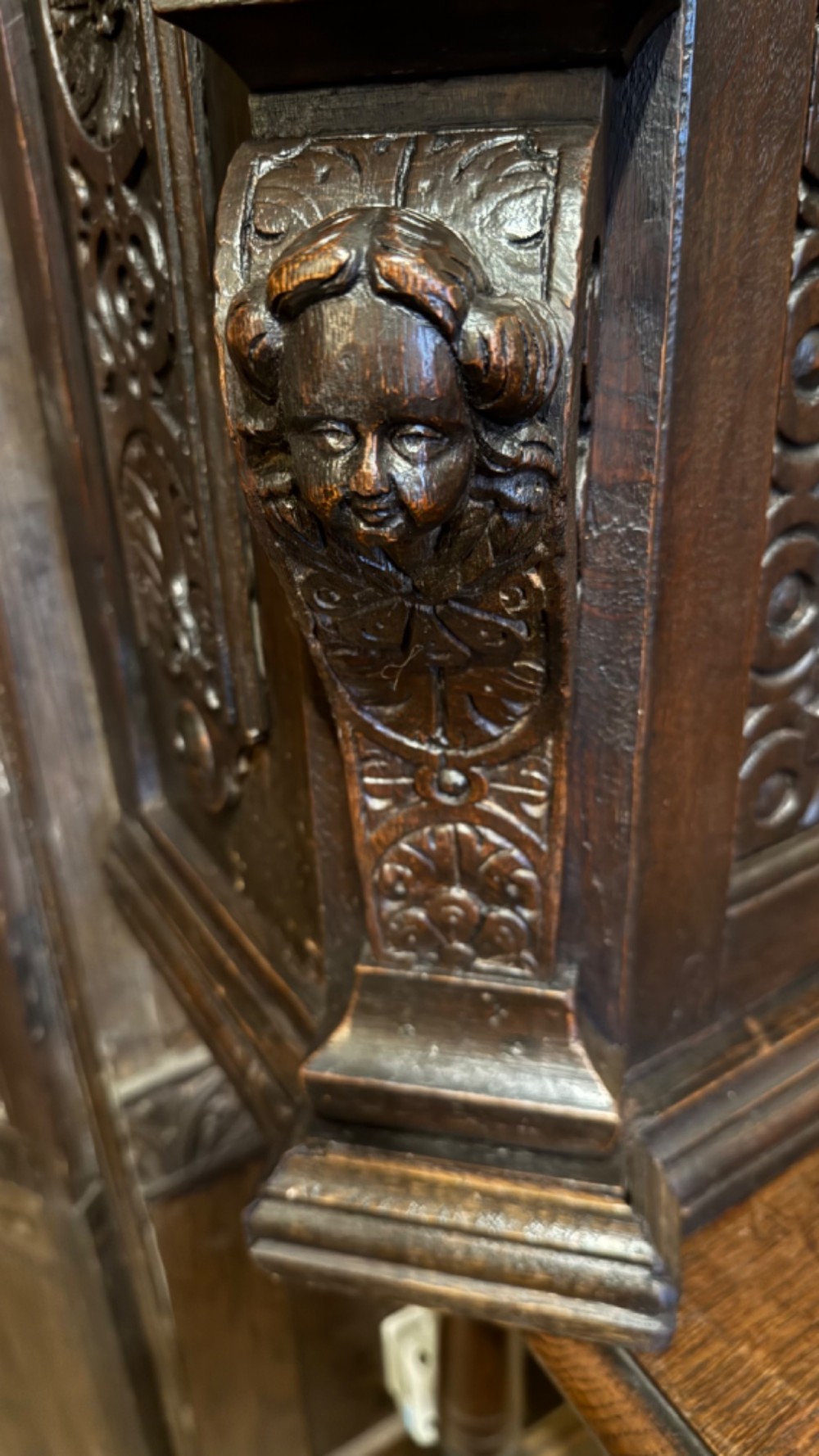 An 18th-century dark oak hanging cupboard featuring carved figural columns, relief door panels with floral motifs, and carved masks. View XI
