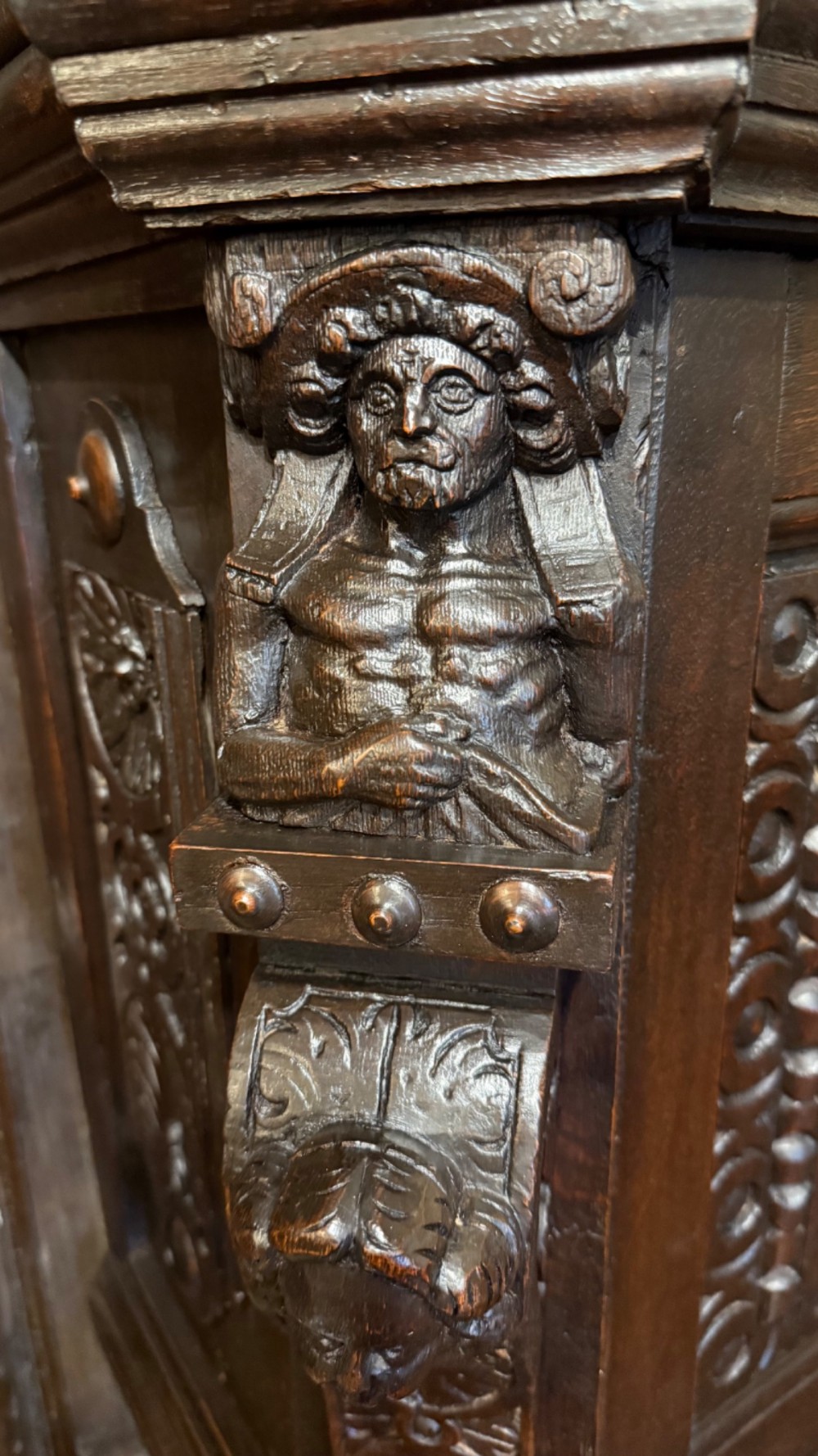 An 18th-century dark oak hanging cupboard featuring carved figural columns, relief door panels with floral motifs, and carved masks. View XII