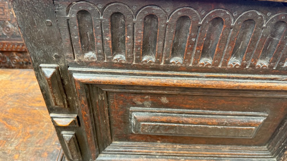 A 17th-century dark oak coffer featuring carved arcaded detail above geometrically moulded panel fronts and a central iron keyhole escutcheon. View V