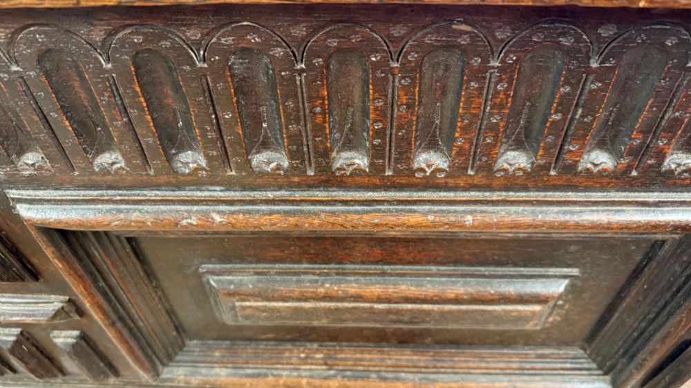 A 17th-century dark oak coffer featuring carved arcaded detail above geometrically moulded panel fronts and a central iron keyhole escutcheon. View VII