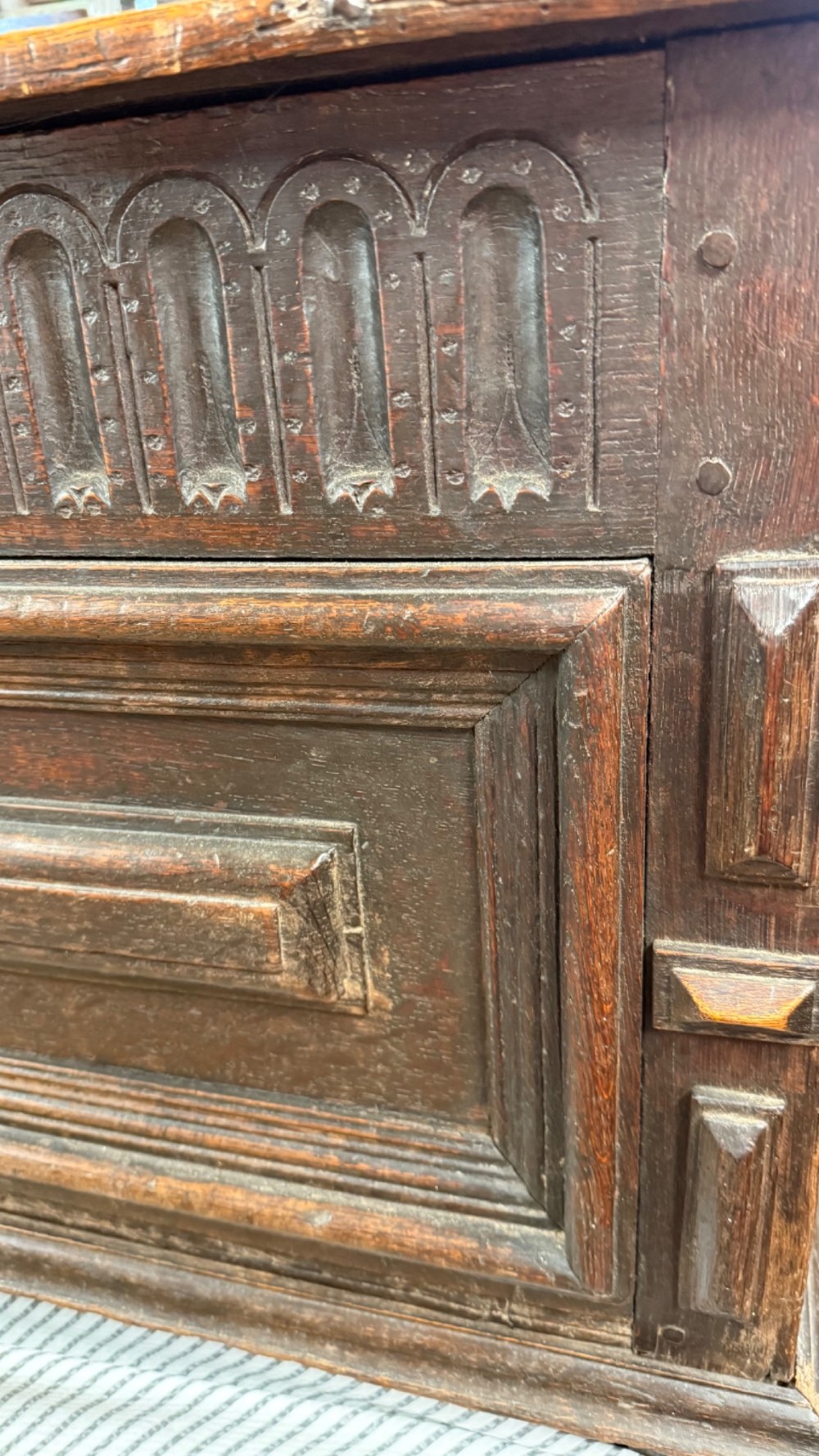 A 17th-century dark oak coffer featuring carved arcaded detail above geometrically moulded panel fronts and a central iron keyhole escutcheon. View VIII