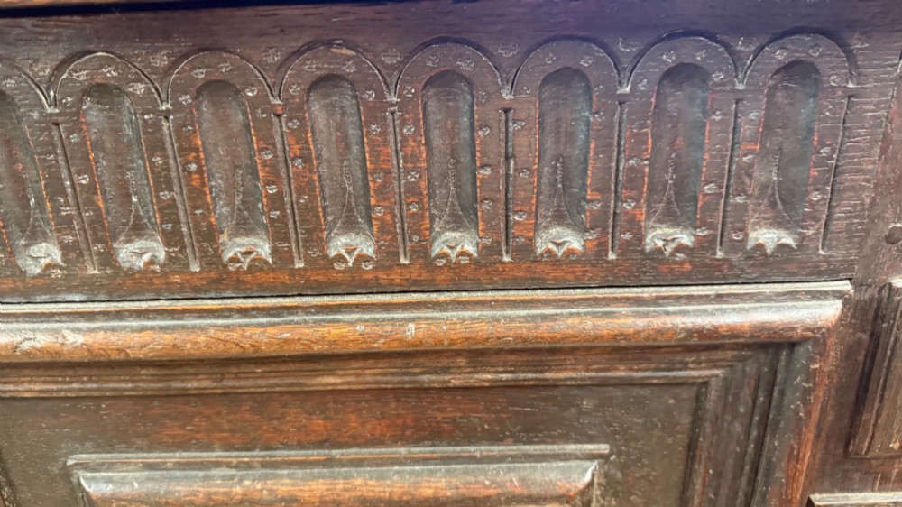 A 17th-century dark oak coffer featuring carved arcaded detail above geometrically moulded panel fronts and a central iron keyhole escutcheon. View IX