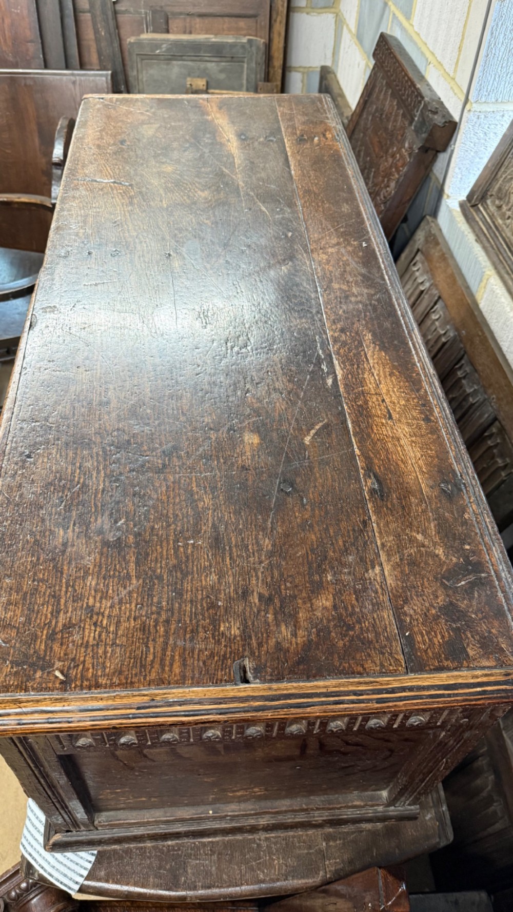 A 17th-century dark oak coffer featuring carved arcaded detail above geometrically moulded panel fronts and a central iron keyhole escutcheon. View XI