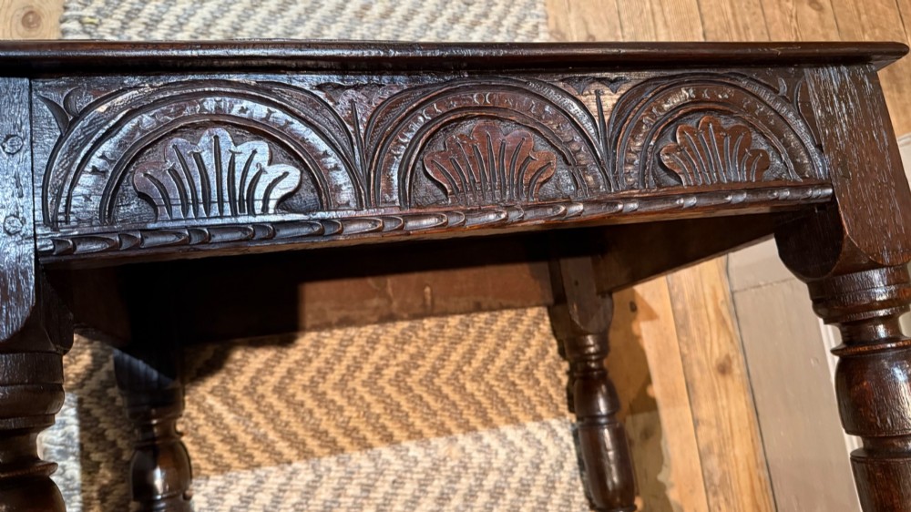 A dark oak 17th-century centre table featuring a carved fan-pattern apron, turned baluster legs, and sturdy wooden stretchers. View XI