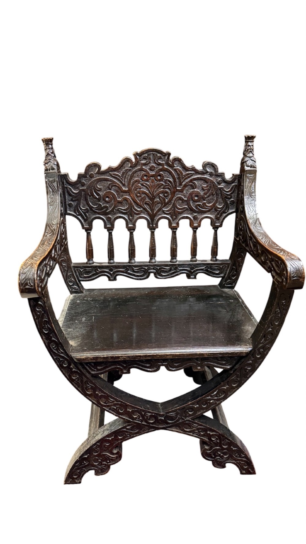 A 19th-century dark carved oak X-frame armchair featuring a foliate backrest, turned balusters, and carved head finials. View II
