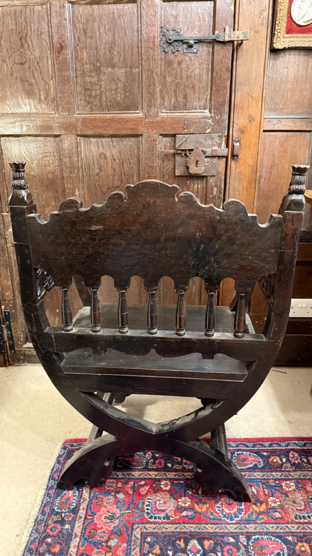 A 19th-century dark carved oak X-frame armchair featuring a foliate backrest, turned balusters, and carved head finials. View V