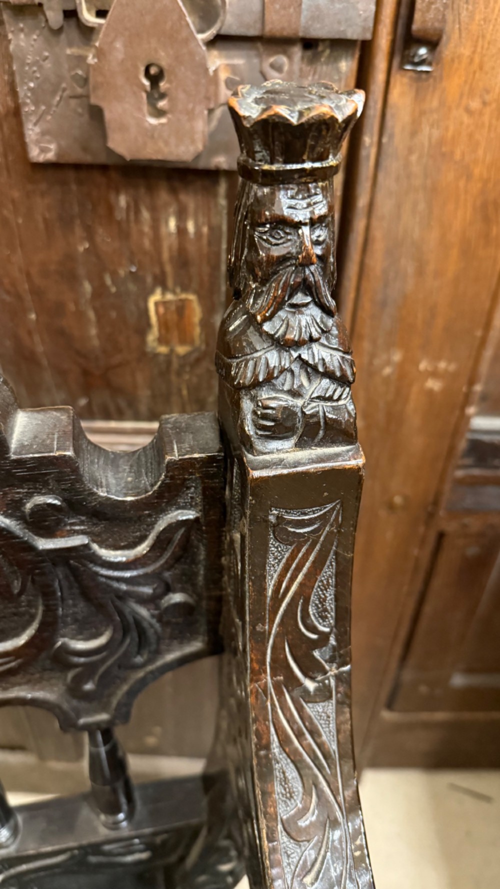 A 19th-century dark carved oak X-frame armchair featuring a foliate backrest, turned balusters, and carved head finials. View VIII