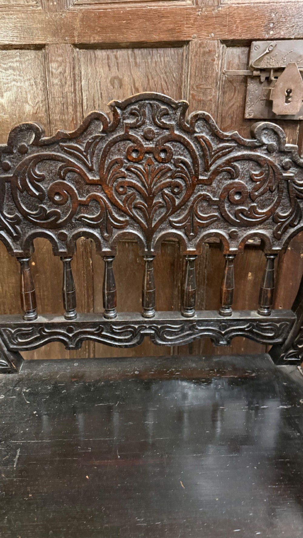 A 19th-century dark carved oak X-frame armchair featuring a foliate backrest, turned balusters, and carved head finials. View XII