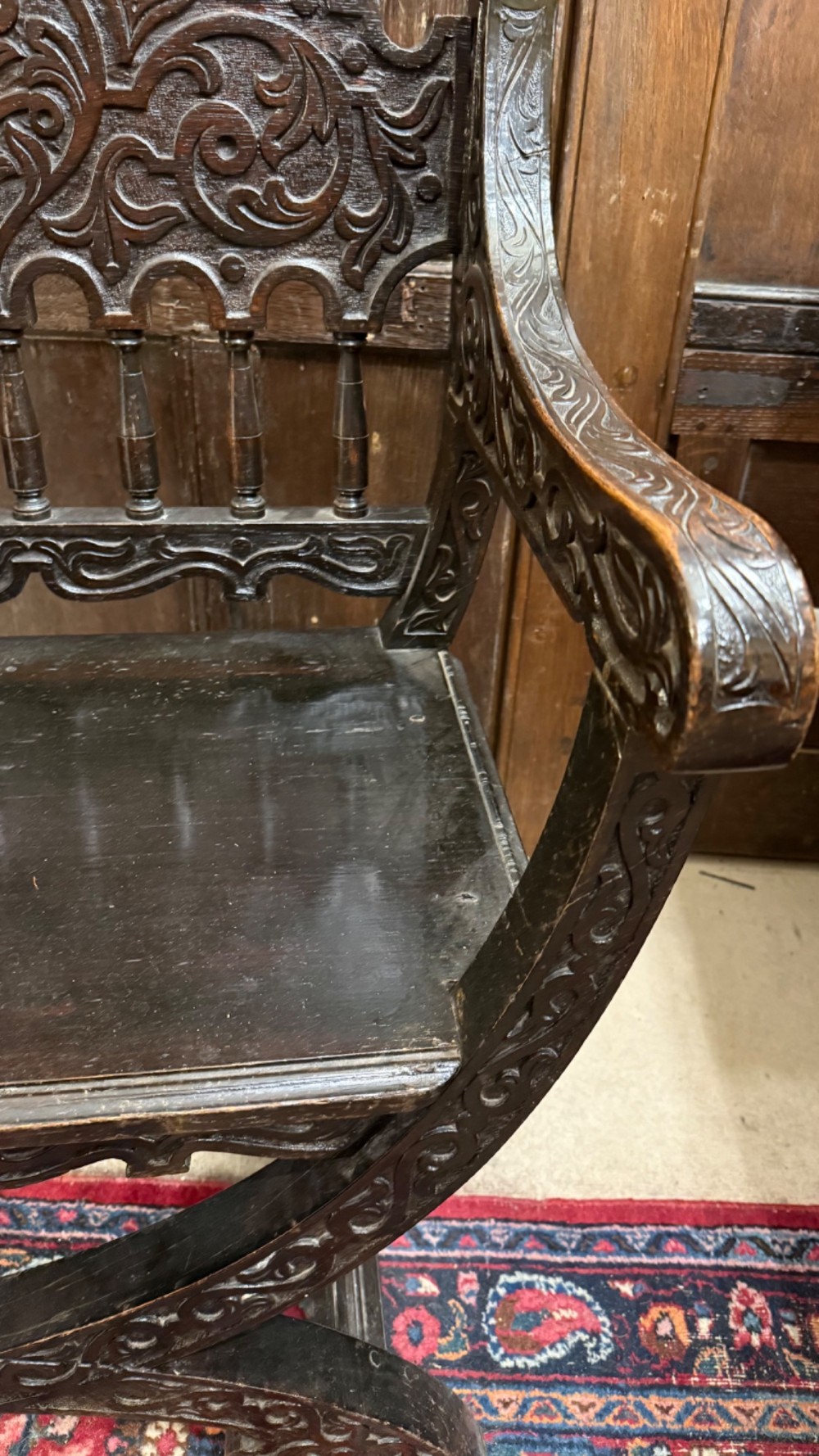 A 19th-century dark carved oak X-frame armchair featuring a foliate backrest, turned balusters, and carved head finials. View XIII