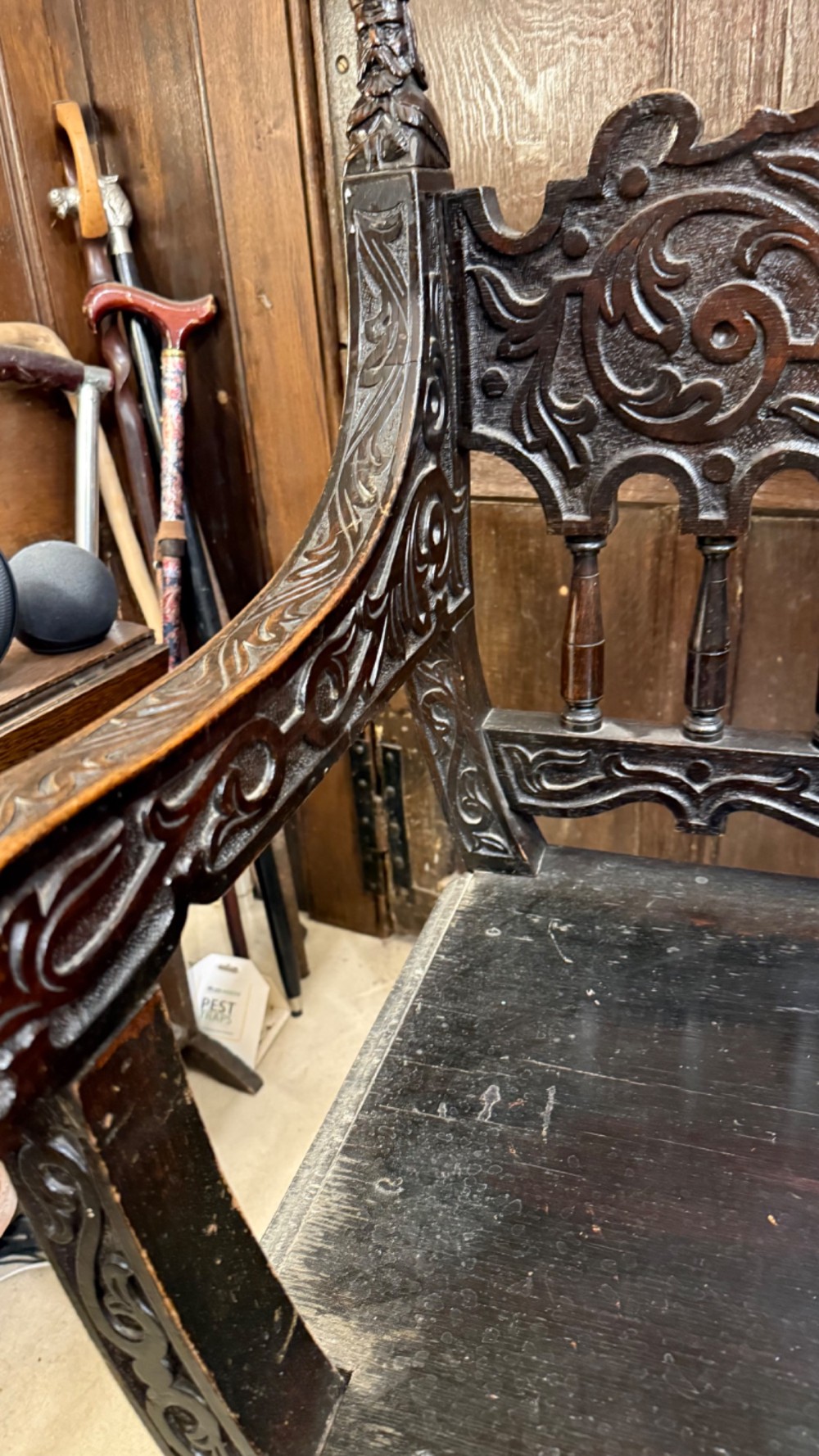 A 19th-century dark carved oak X-frame armchair featuring a foliate backrest, turned balusters, and carved head finials. View XIV