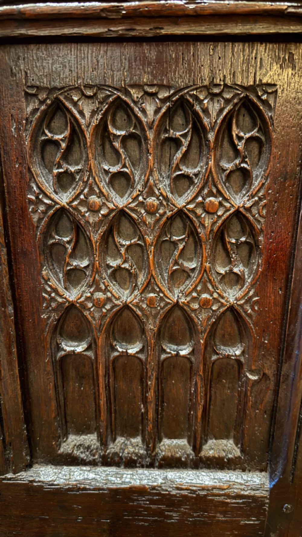 A dark brown 16th-century oak coffer featuring three front panels carved with gothic tracery and a central iron lockplate. View IV