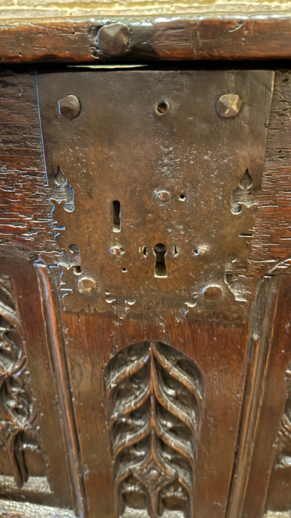 A dark brown 16th-century oak coffer featuring three front panels carved with gothic tracery and a central iron lockplate. View V