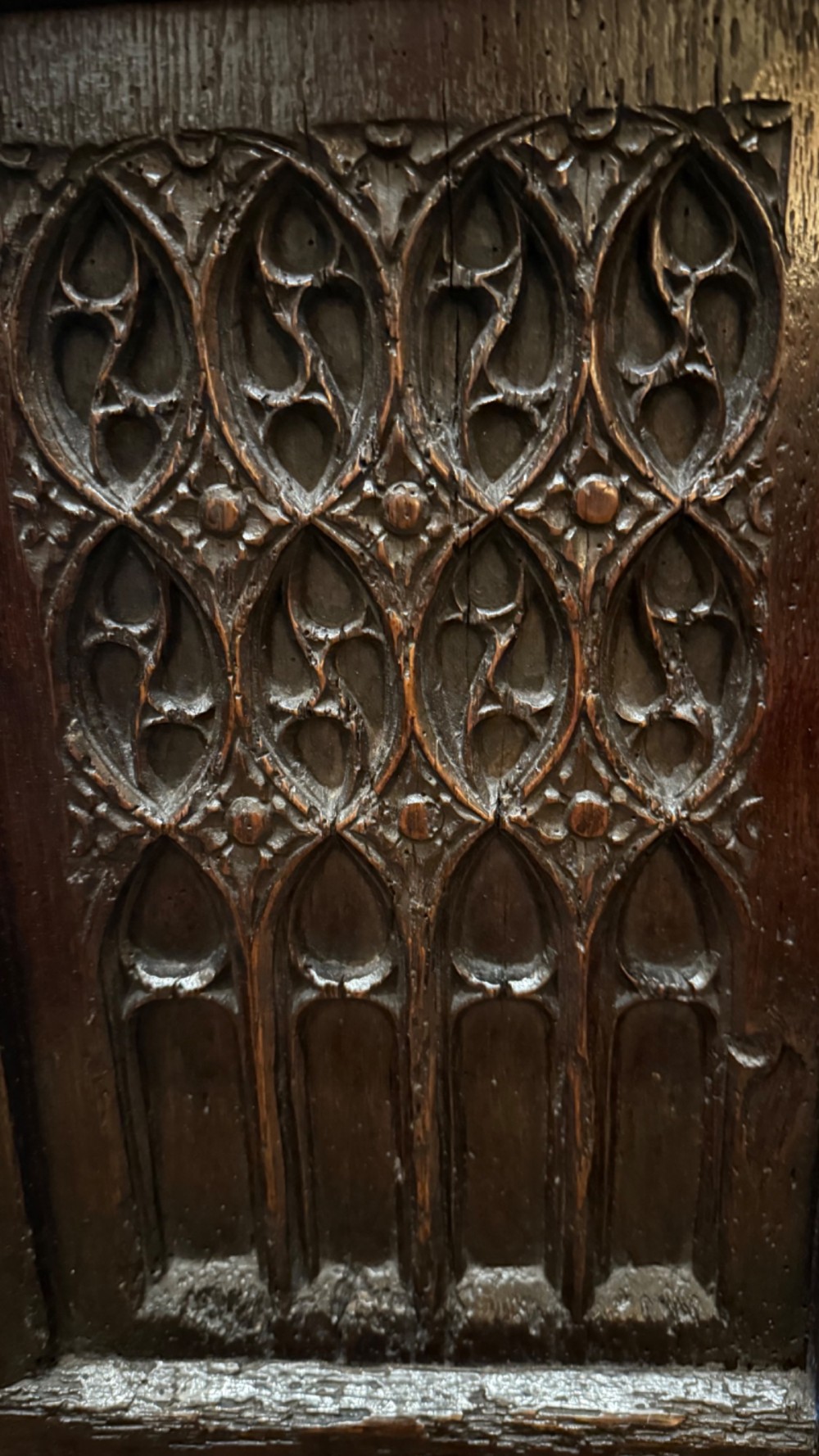 A dark brown 16th-century oak coffer featuring three front panels carved with gothic tracery and a central iron lockplate. View VII