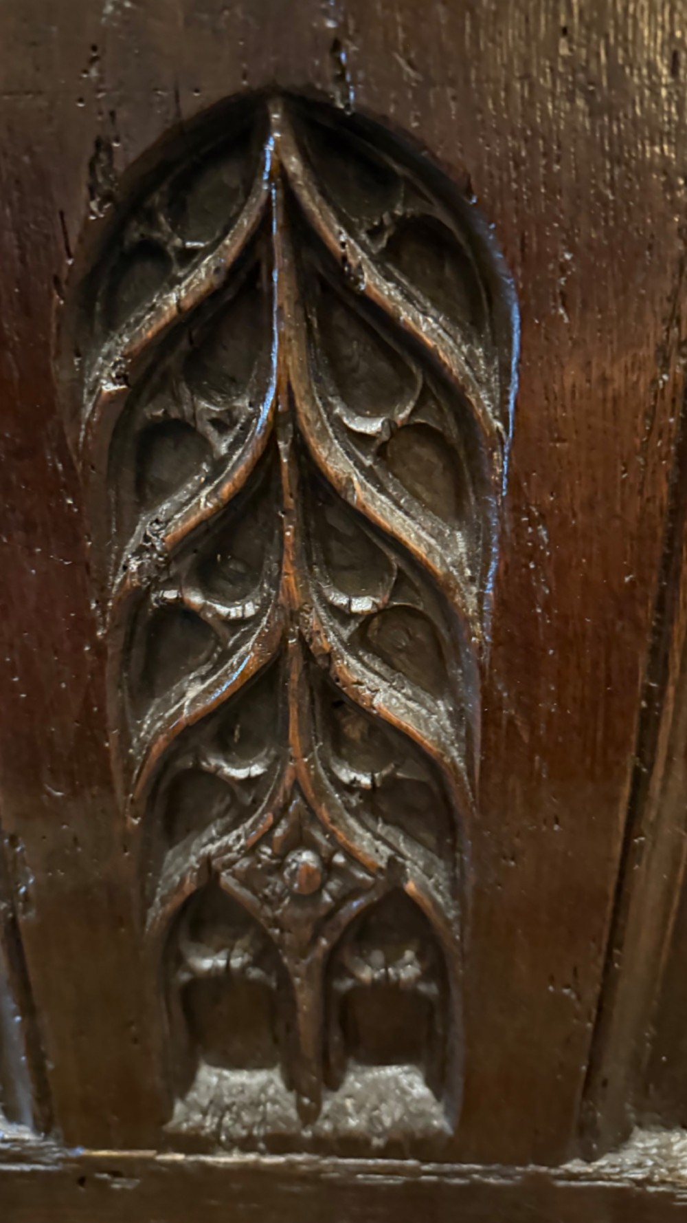A dark brown 16th-century oak coffer featuring three front panels carved with gothic tracery and a central iron lockplate. View VIII