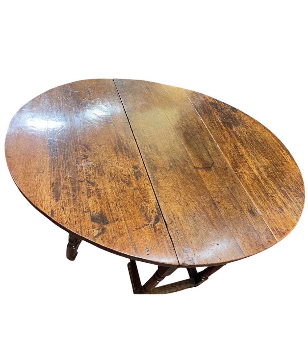 An 18th-century walnut gateleg table featuring an oval drop-leaf top supported by turned legs.
