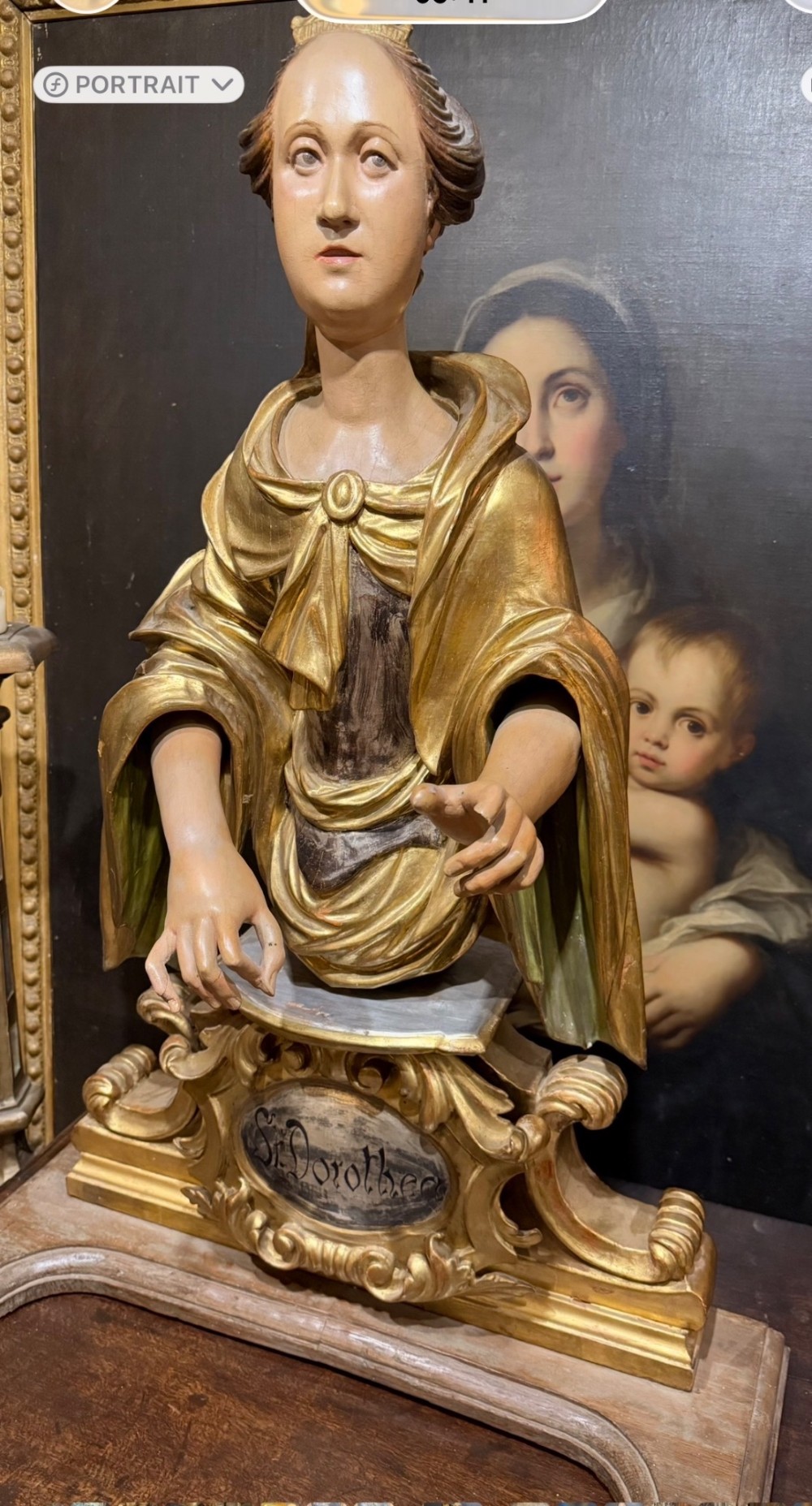 A seventeenth-century carved wooden bust of Saint Dorothea featuring gilded drapery and polychrome painted skin tones mounted on a decorative cartouche base. View XII