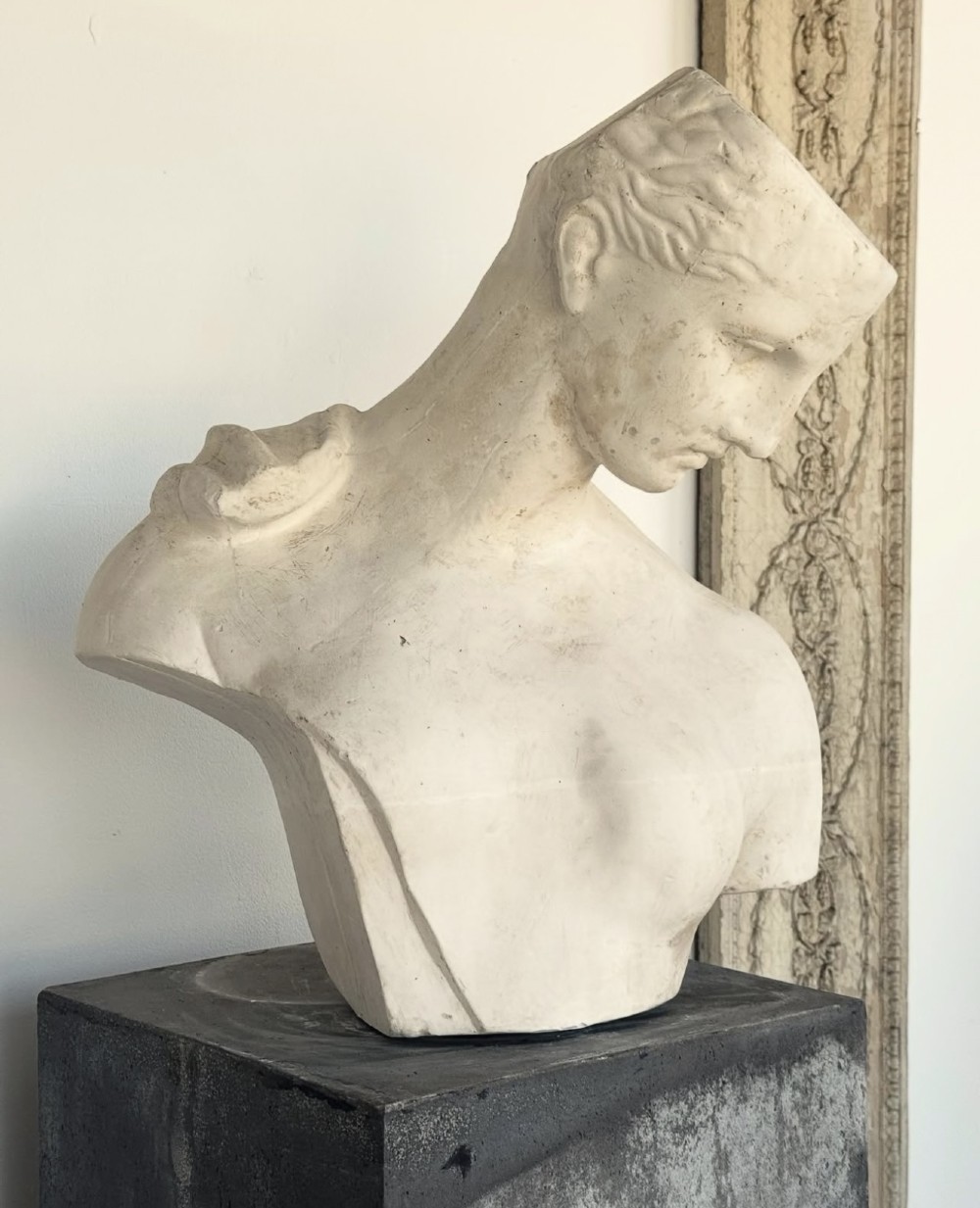 An off-white plaster bust depicting a classical head and torso in profile, angled downwards against a neutral background.