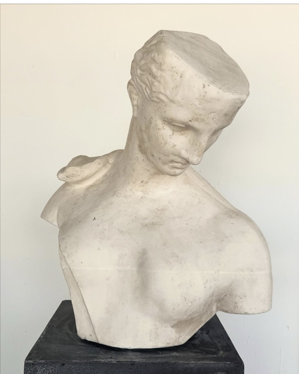 An off-white plaster bust depicting a classical head and torso in profile, angled downwards against a neutral background. View II