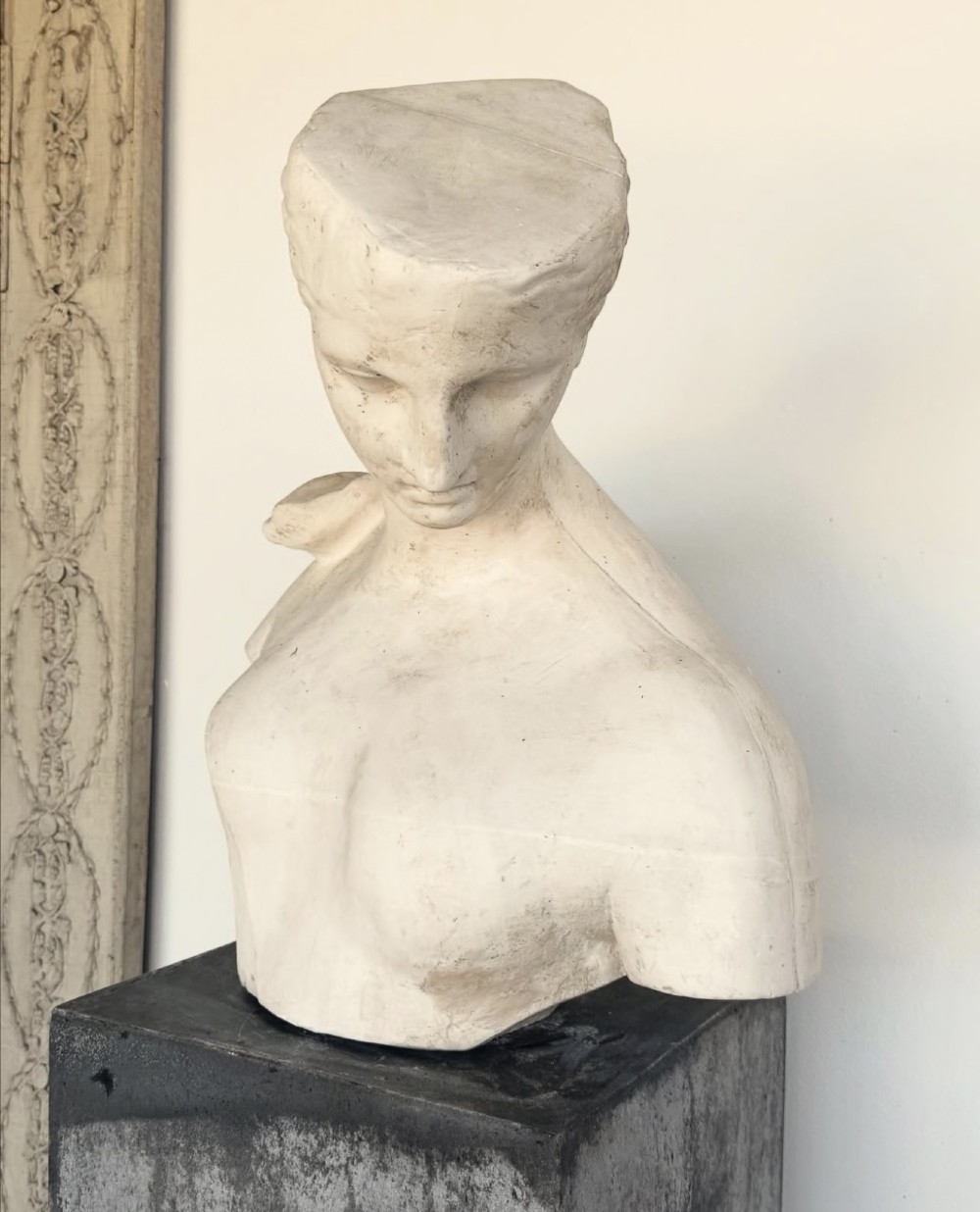 An off-white plaster bust depicting a classical head and torso in profile, angled downwards against a neutral background. View III