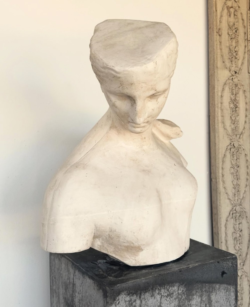 An off-white plaster bust depicting a classical head and torso in profile, angled downwards against a neutral background. View VI