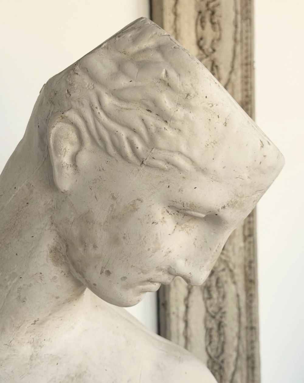 An off-white plaster bust depicting a classical head and torso in profile, angled downwards against a neutral background. View VII
