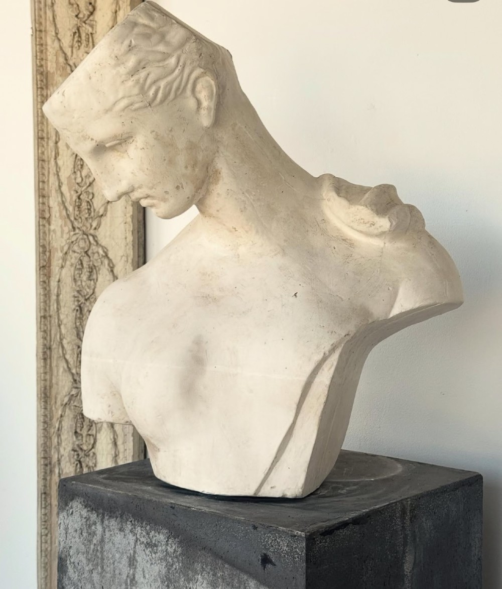 An off-white plaster bust depicting a classical head and torso in profile, angled downwards against a neutral background. View X
