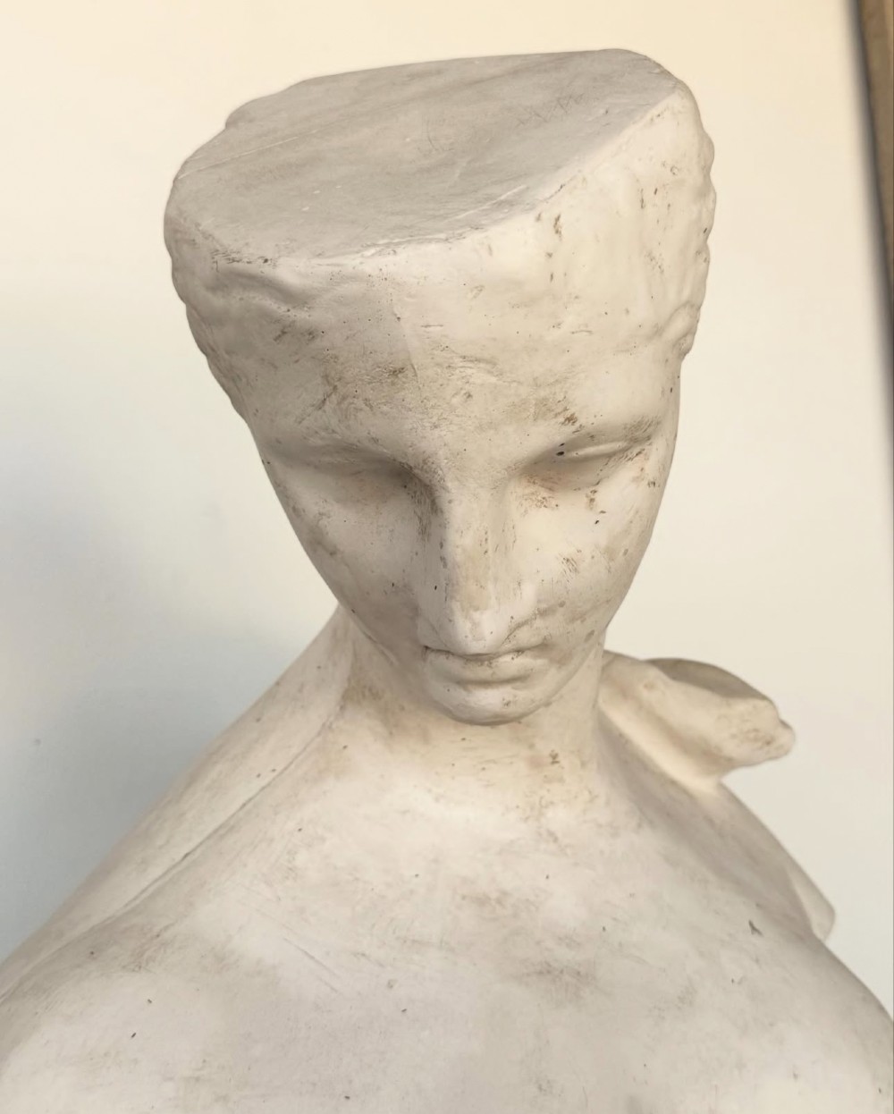 An off-white plaster bust depicting a classical head and torso in profile, angled downwards against a neutral background. View XII