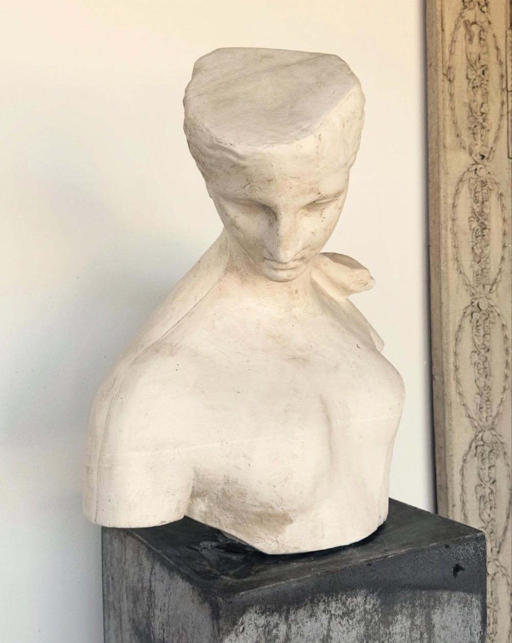 An off-white plaster bust depicting a classical head and torso in profile, angled downwards against a neutral background. View XIV