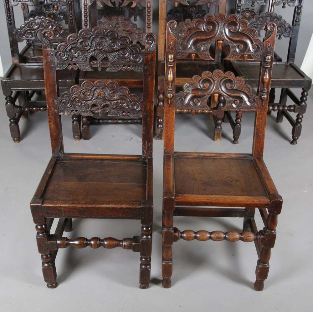 A set of dark carved oak dining chairs featuring carved openwork backs with scroll motifs, solid wooden seats, and turned front legs. View II