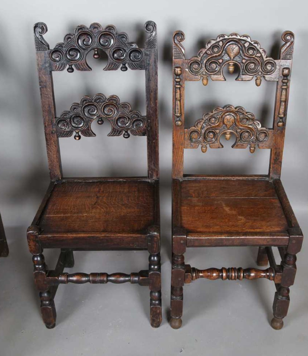 A set of dark carved oak dining chairs featuring carved openwork backs with scroll motifs, solid wooden seats, and turned front legs. View III