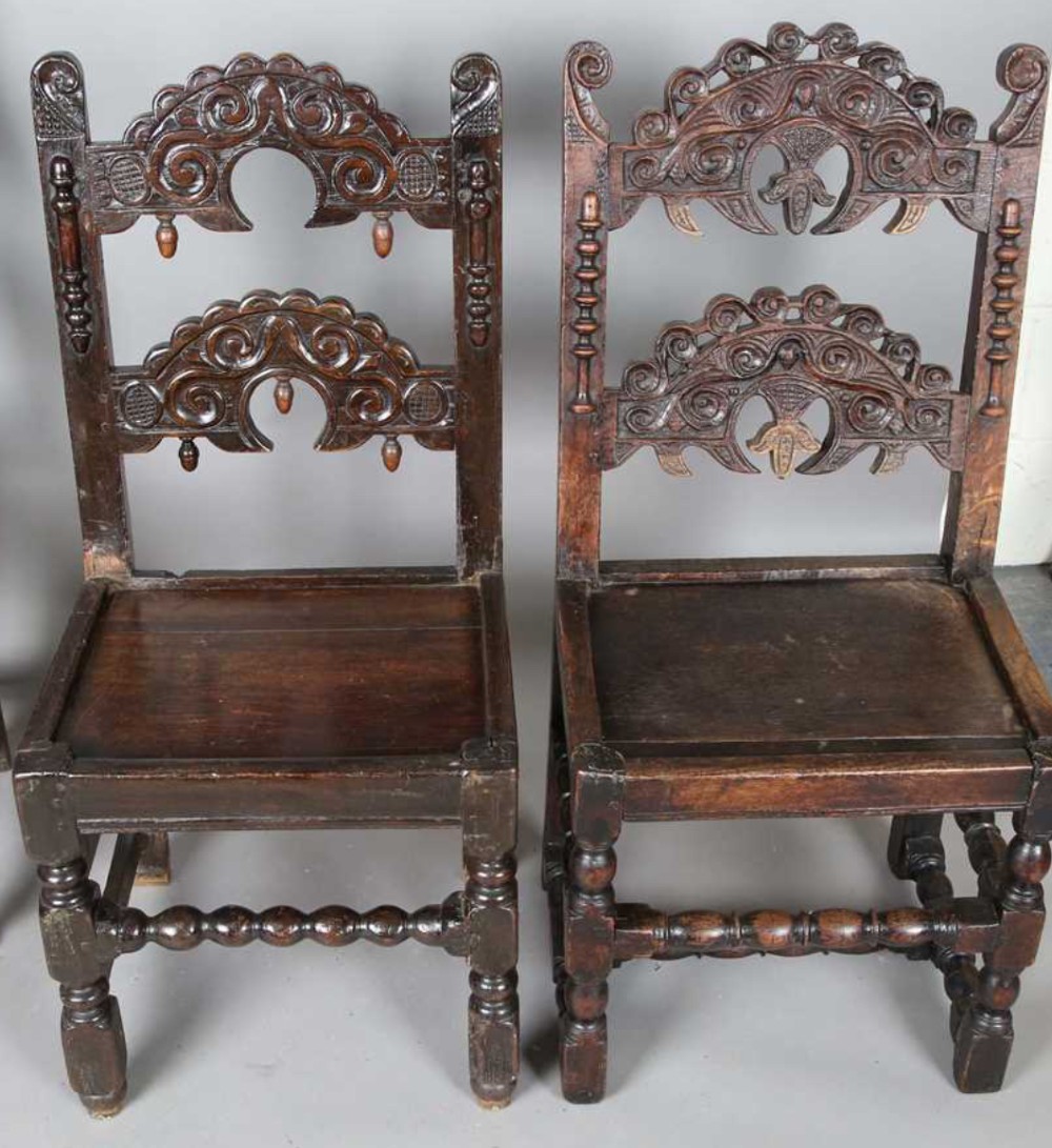 A set of dark carved oak dining chairs featuring carved openwork backs with scroll motifs, solid wooden seats, and turned front legs. View V
