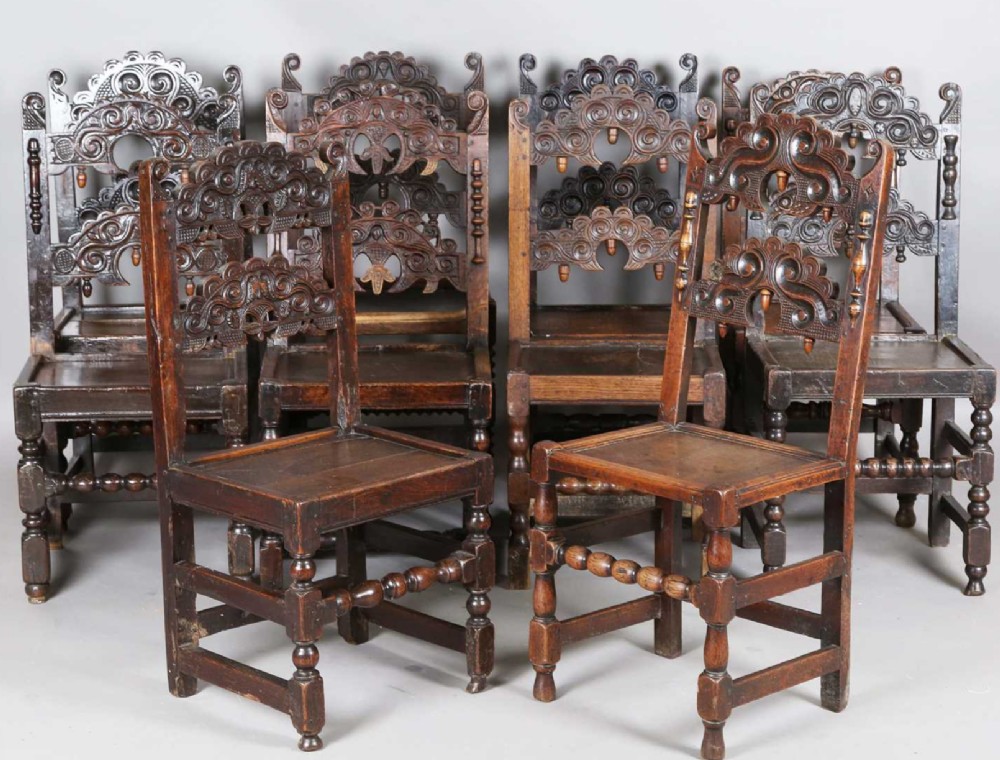 A set of dark carved oak dining chairs featuring carved openwork backs with scroll motifs, solid wooden seats, and turned front legs. View VII