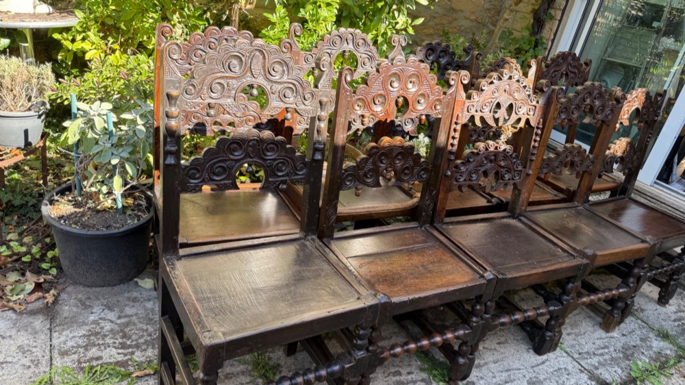 A set of dark carved oak dining chairs featuring carved openwork backs with scroll motifs, solid wooden seats, and turned front legs. View XIII